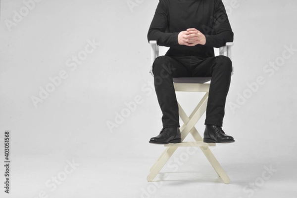 Obraz A man without a face in black clothes sits in the director's chair on a white background in the studio