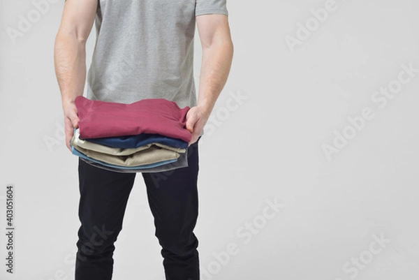 Obraz A man in the studio on a white background without a face holds a stack of clothes in his hands