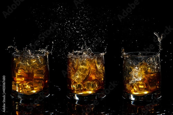 Fototapeta set of three glasses of scotch whiskey with splash and ice on black background
