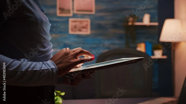 Fototapeta Close up of african employee texting, sending and reading messages during her break standing in living room late at night. Focused black employee using modern technology network wireless overworking