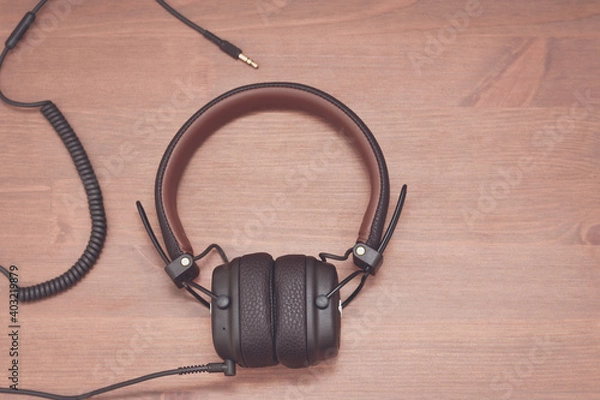 Fototapeta Brown design headphones with wire on wooden background.
