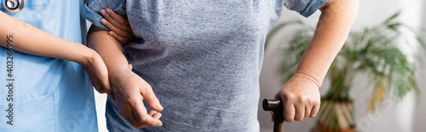 Fototapeta partial view of nurse supporting aged woman with walking stick, banner