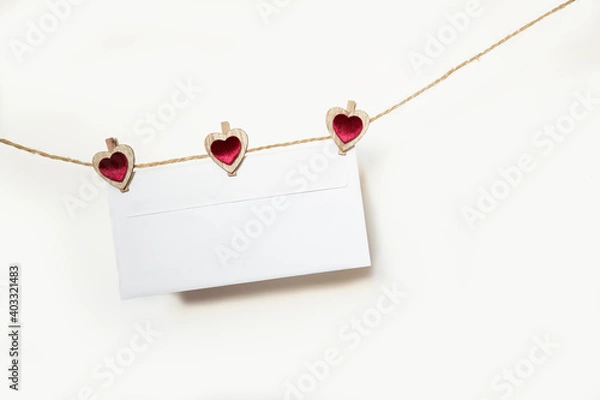 Obraz Blank envelope hanging on a rope with clothespins in the shape of hearts on a white background on valentine's day february 14. Place for text.