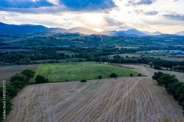 Fototapeta Aerial view of warm sunset on the hills surrounding Fabriano, Marche, Italy. It's summer and the sun is lighting the cultivated fields.