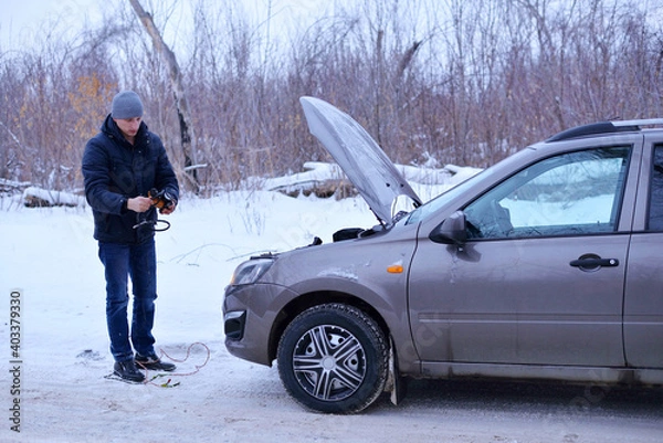Obraz car repair on the road in winter. a young man is trying to fix a car breakdown under the soot on the road. woodsroadside assistance car