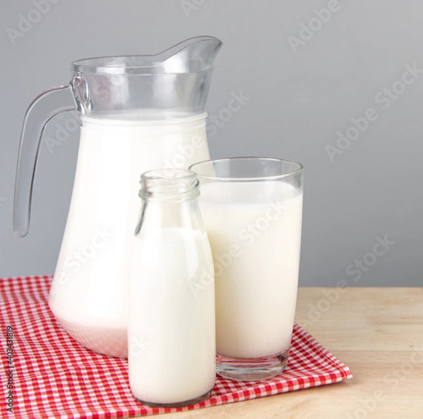 Fototapeta  A jug and bottle of milk glass on a wooden table on background..Raw milk is high in calcium and protein to drink for all ages..Milk consumption nutritious and healthy dairy products concept..