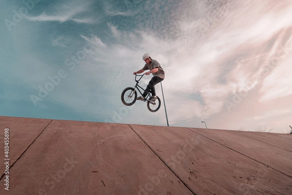 Obraz young bmx rider wearing a white helmet jumping on a ramp with the bike