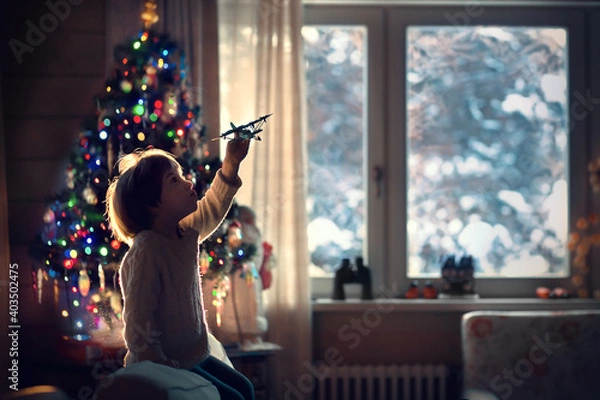 Fototapeta Little boy is playing with a plane near the new year tree. Image with selective focus.