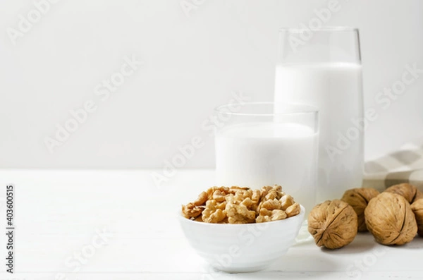 Fototapeta Milk from walnuts and nuts on a white wooden background. Products containing vegetable protein, vitamins, and useful amino acids. Copy space.