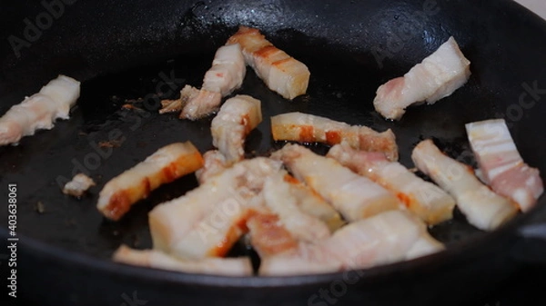 Obraz Fried pieces of bacon in a black pan.Pork belly close-up.