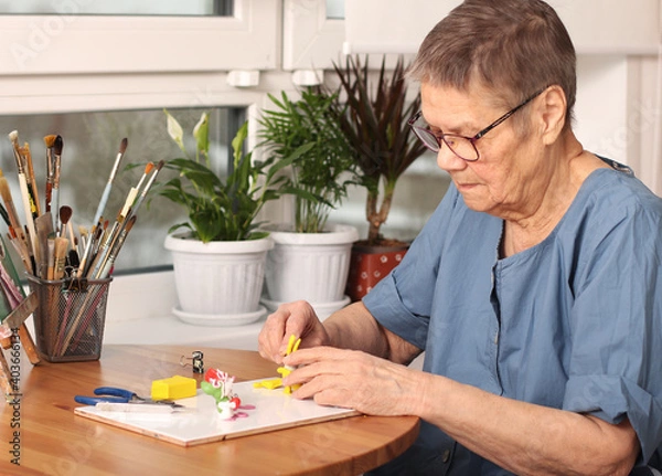 Fototapeta Active old age. An elderly woman sculpts small toys from polymer clay. Art therapy. the age of 80 years. A happy elderly person is engaged in creativity