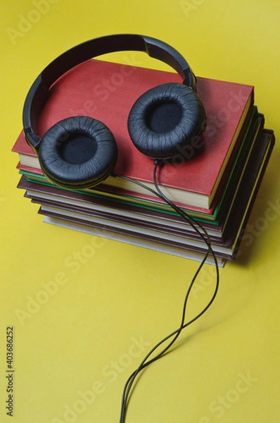 Fototapeta on a yellow background are a stack of books and large, black headphones.