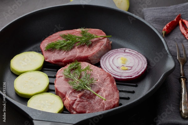 Fototapeta Beef steaks and cutting vegetables on grill pan on black slate background. Steak menu