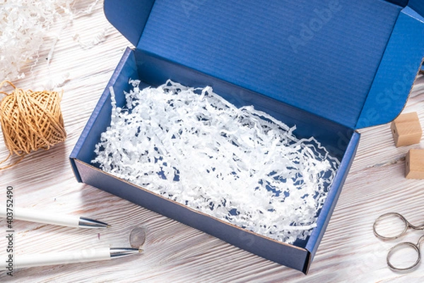 Fototapeta Blue carton cardboard box with paper filler, top view, isolated