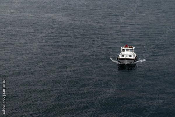 Fototapeta Small white ship with red flag is sailing in the sea. Pleasure touristic yacht or fishing boat.