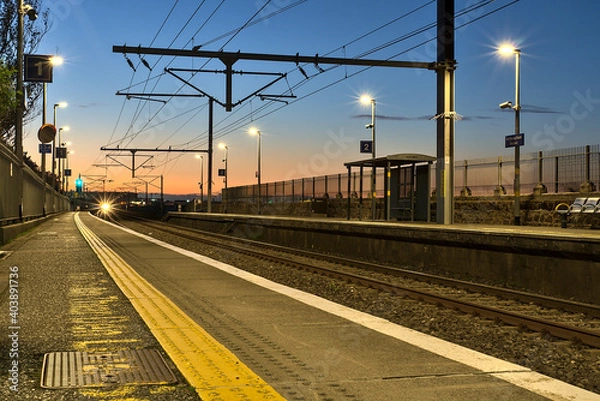 Fototapeta Spectacular view of railway station and colorful sky at Blackrock in the evening, Dublin, Ireland. Lights of the coming train in background