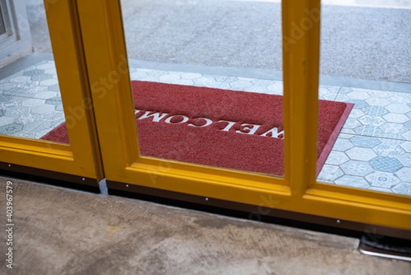 Obraz Welcome red mat greeting all visitors in front of a yellow glass door for  shop and restaurant in a shopping mall.