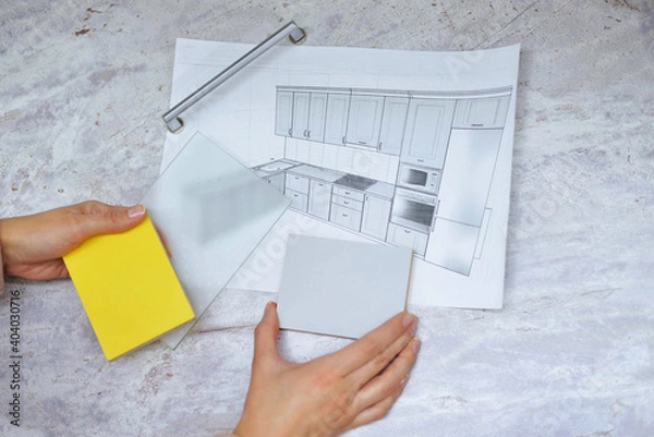 Fototapeta soft focus On the table is a mock-up of a kitchen, an example of a palette of facades and drawer bodies and a handle for the door. girl orders furniture for the kitchen in the salon. close-up
