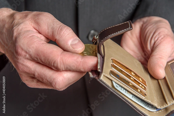 Fototapeta A man in a suit holds a bitcoin in his hand. Men's hands take out or put a bill in a wallet.