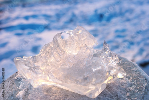 Obraz A piece of ice of unusual shape in the sunlight, against the background of a frozen river. Close-up, side view. Space for text