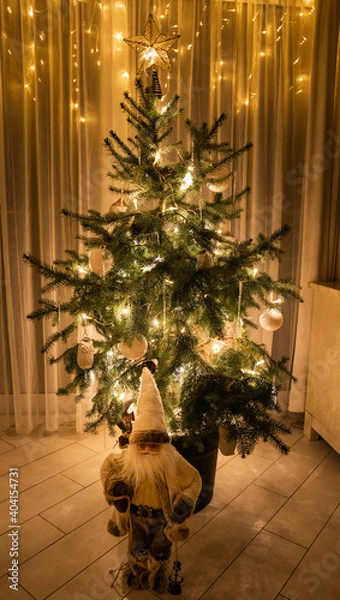 Fototapeta Christmas Tree with lights and Santa Claus figure in a low-light room