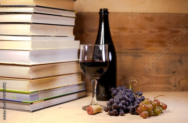 Obraz A glass of red wine with grapes, books and bottle