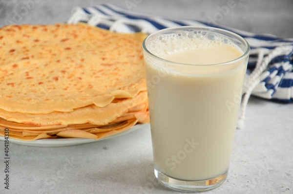 Fototapeta A glass of milk on a stone gray table, next to a plate of crepes.