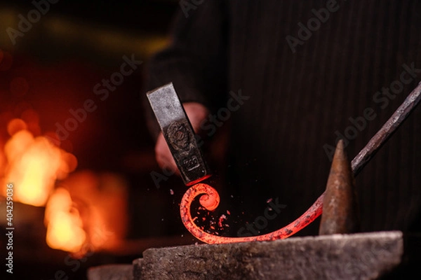 Fototapeta Blacksmithing. The blacksmith on the anvil measures the width of the split product and glowing sparks fly in all directions. Photo of red metal close-up.