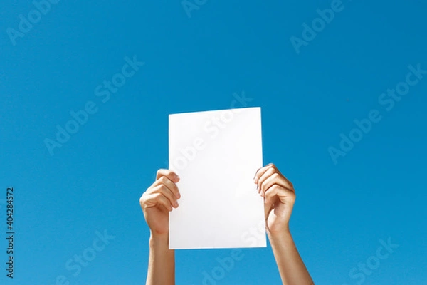 Fototapeta blank sheet of paper in hands on blue background