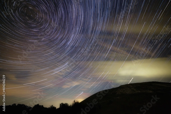 Obraz A trail of bright stars from the Milky Way in the cloudy night sky over the hills.