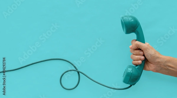 Obraz A blue-green vintage dial telephone handset with one hand and blue-green background. 