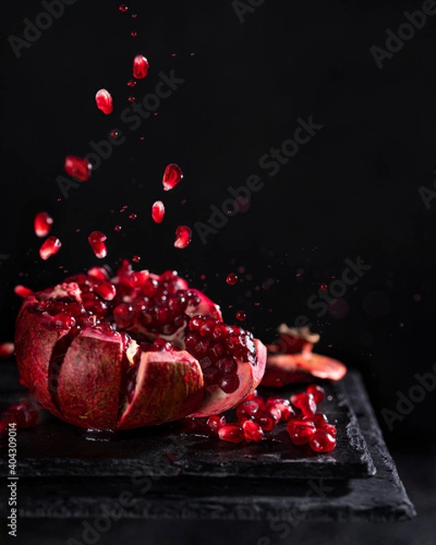 Fototapeta Freeze motion of sliced pomegranate red fruit with splashing juice, drops and seeds on black background. Copy space.