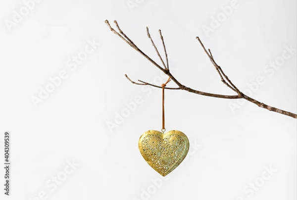 Obraz Gold patterned metal heart on a string hanging on a bare winter tree branch against a white background for valentine's day february 14