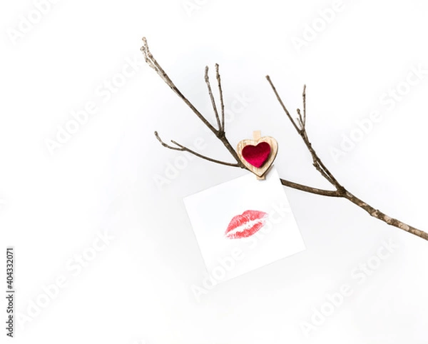 Obraz White card with lip print hanging on a bare winter tree branch pinned with a clothespin with a red heart for Valentine's Day. On white background isolated