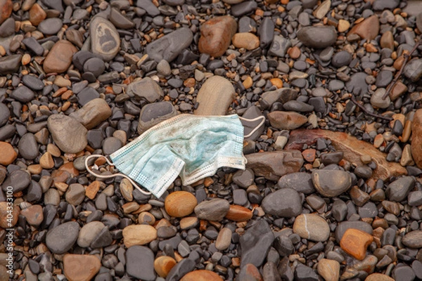 Fototapeta Discarded used medical grade polypropylene face mask found on a sea beach creates a new form of environmental pollution. Pollution concept.