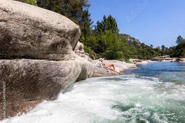 Obraz Woman with hat sunbathing along a river lying on a rock