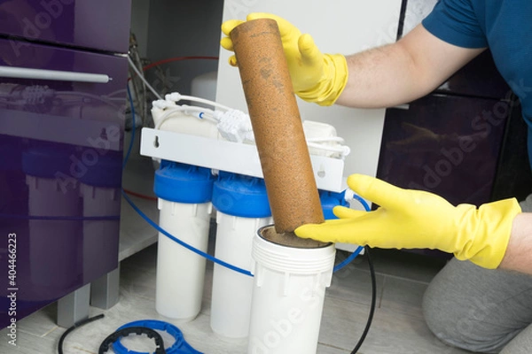 Fototapeta Plumber in yellow household gloves changes water filters. Repairman installing water filter cartridges in kitchen. Drinkable water filtration system in the kitchen. Clean water at home
