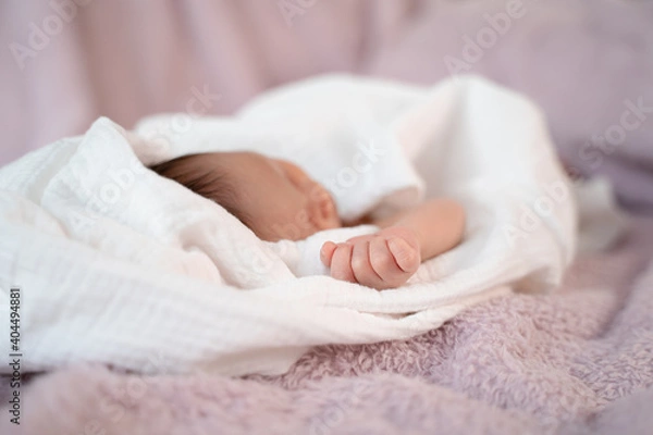 Fototapeta close up small hand of baby infant sleeping on soft bed covered with white cloth. little baby fingers in fist.
