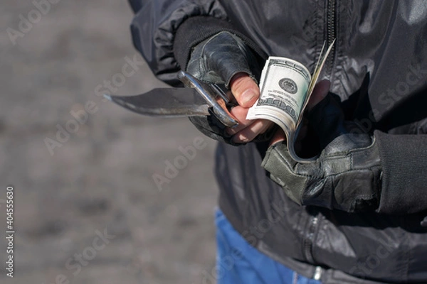 Fototapeta close up, the hands of a bandit in leather gloves holding a knife and counting banknotes, dollars on the street