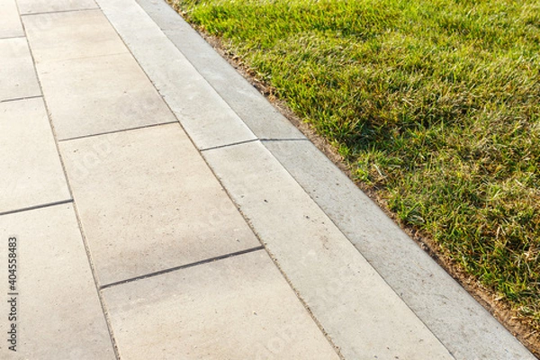 Fototapeta Smooth transition of the sidewalk paved with concrete tiles into the lawn.
