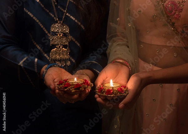 Fototapeta Two pairs of hands holding Deepawali Diya or illuminated stylish and decorative lamps during a prayer ceremony at the onset of Deepawali festival which marks the victory of good over evil.