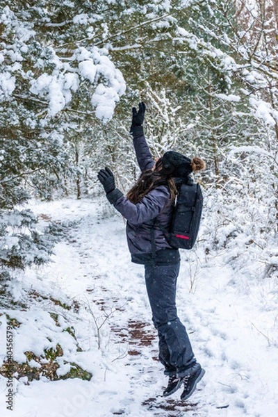 Fototapeta Young girl jumping to hit the snow on the branches of the trees in the forest.