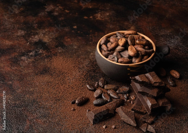 Fototapeta Chocolate and cacao concept. Cocoa powder in bowl near cocoa beans and broken chocolate on black background