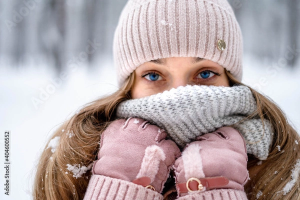 Obraz a girl with blue eyes in a winter forest looks straight dressed in pink gloves, a pink hat and a jacket