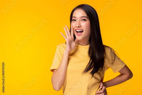 Fototapeta Surprised happy beauty asian woman look at camera in excitement Expressive facial expressions Presenting some product Beautiful girl act like a telling something Isolated on yellow background
