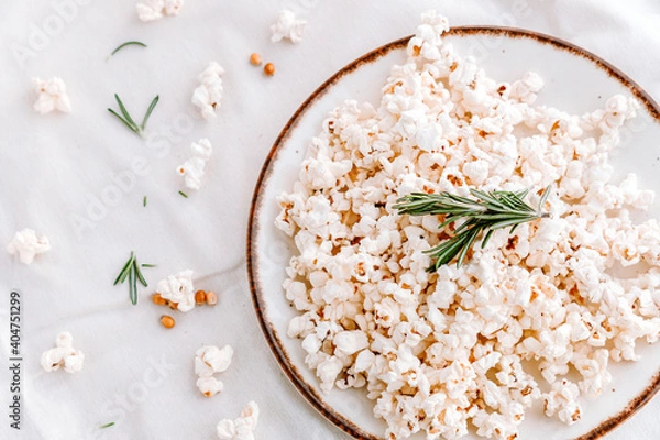 Fototapeta Popcorns with corn and rosemary on a dish isolated on white edited with warm tones. Top view