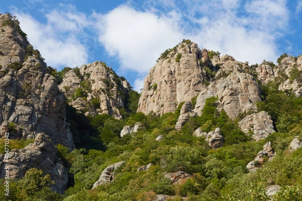Fototapeta steep mountains with forest at the bottom against a blue cloudy sky