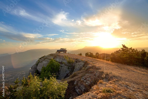 Fototapeta Jeep near a steep cliff against the background of mountains and the setting sun in the blue sky