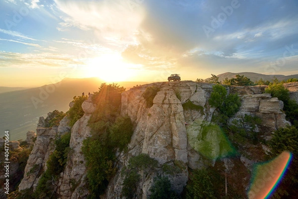Fototapeta Jeep near a steep cliff against the background of mountains and the setting sun in the blue sky