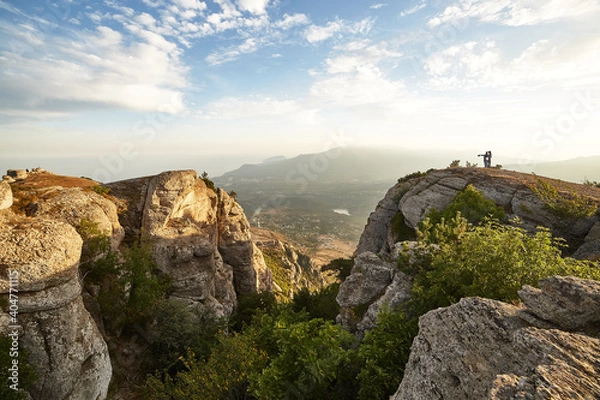 Fototapeta steep cliff in the rocks against the background of mountains and cloudy blue sky